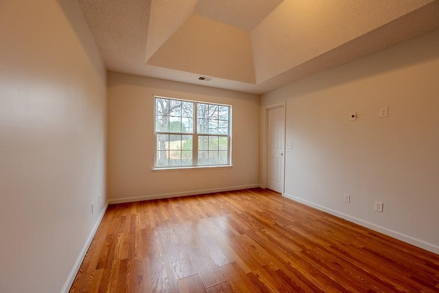 empty room with light wood-type flooring, visible vents, a tray ceiling, a textured ceiling, and baseboards