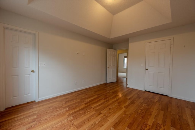 unfurnished bedroom with light wood-style flooring, a tray ceiling, baseboards, and vaulted ceiling