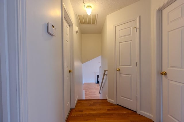 hallway featuring visible vents, a textured ceiling, baseboards, and wood finished floors