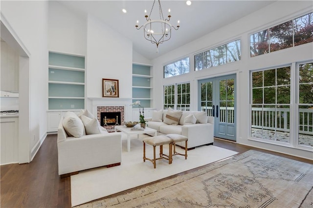 living room featuring a chandelier, dark wood-type flooring, a brick fireplace, high vaulted ceiling, and built in features