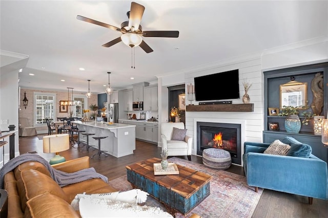 living area with a glass covered fireplace, recessed lighting, ceiling fan, and dark wood-style flooring