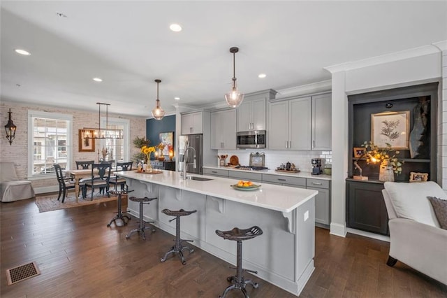 kitchen featuring a kitchen bar, appliances with stainless steel finishes, gray cabinetry, a sink, and light countertops