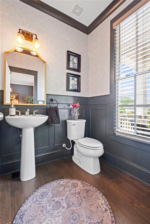 bathroom featuring toilet, visible vents, hardwood / wood-style flooring, and a wainscoted wall