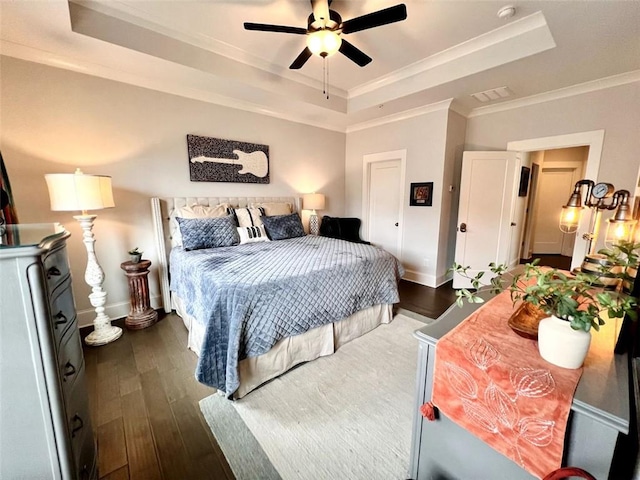 bedroom with crown molding, a tray ceiling, dark wood finished floors, and baseboards