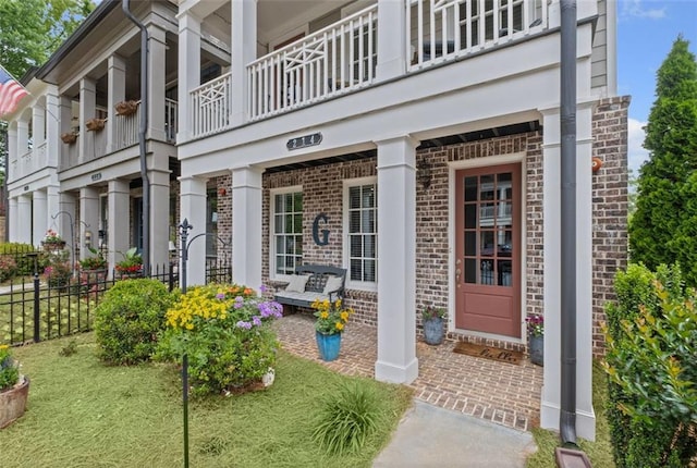 doorway to property featuring a balcony, fence, and brick siding