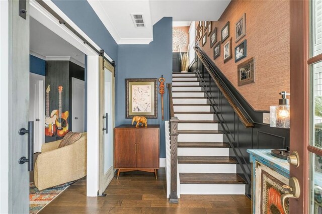 staircase with ornamental molding, visible vents, a barn door, and wood finished floors