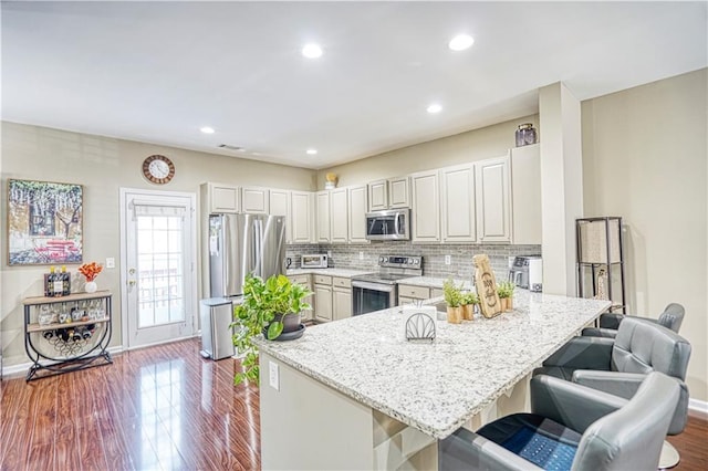 3068 Cedar Glade Ln, Buford, GA 30519 - kitchen with appliances with stainless steel finishes, a kitchen breakfast bar, tasteful backsplash, wood-type flooring, and light stone countertops