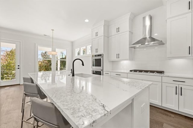 1005 Coleman Place Dr, Roswell, GA 30075 - kitchen featuring wall chimney exhaust hood, stovetop, double oven, an island with sink, and wood finished floors