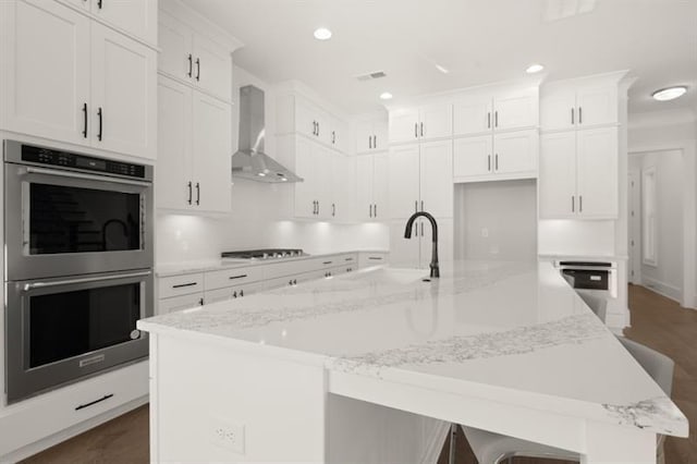 1005 Coleman Place Dr, Roswell, GA 30075 - kitchen with stainless steel double oven, wall chimney range hood, stovetop, white cabinetry, and a spacious island