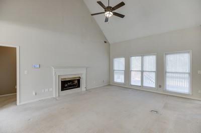 unfurnished living room with light carpet, high vaulted ceiling, and ceiling fan