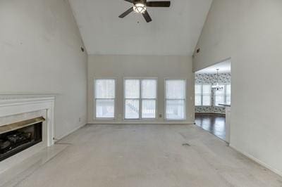 unfurnished living room featuring ceiling fan with notable chandelier and high vaulted ceiling