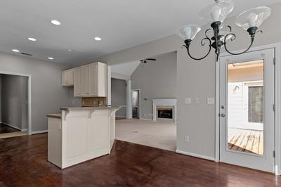 kitchen with a chandelier, vaulted ceiling, dark carpet, kitchen peninsula, and white cabinetry