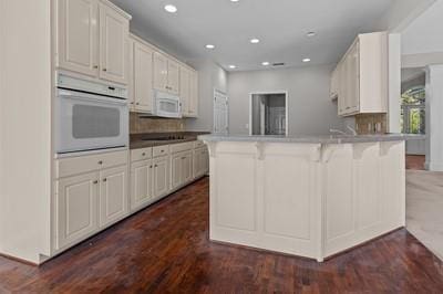 kitchen with white cabinets, white appliances, dark wood-type flooring, a kitchen bar, and decorative backsplash