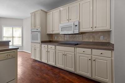 kitchen with dark wood-type flooring, decorative backsplash, white appliances, and white cabinetry