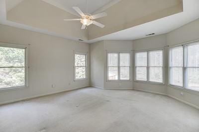 carpeted spare room with ceiling fan, plenty of natural light, and a raised ceiling