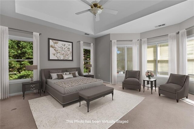 carpeted bedroom with ceiling fan, a tray ceiling, and multiple windows