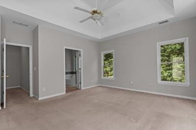 unfurnished bedroom with light carpet, a raised ceiling, connected bathroom, and ceiling fan