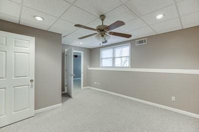 basement featuring a paneled ceiling, ceiling fan, and light colored carpet