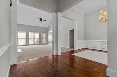 unfurnished living room featuring ceiling fan with notable chandelier, high vaulted ceiling, dark colored carpet, and decorative columns