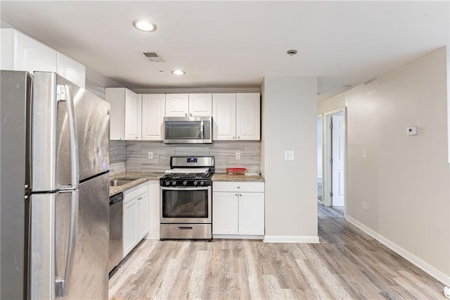 kitchen with stainless steel appliances, tasteful backsplash, white cabinetry, light wood-type flooring, and baseboards