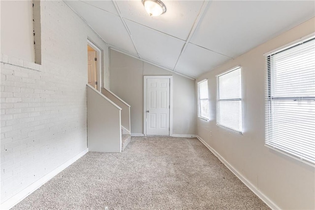 empty room with lofted ceiling, brick wall, carpet flooring, baseboards, and stairs