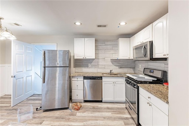 kitchen with stainless steel appliances, a sink, visible vents, light stone countertops, and light wood finished floors