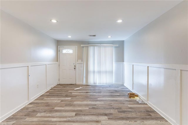 entrance foyer with wainscoting, wood finished floors, visible vents, and a decorative wall