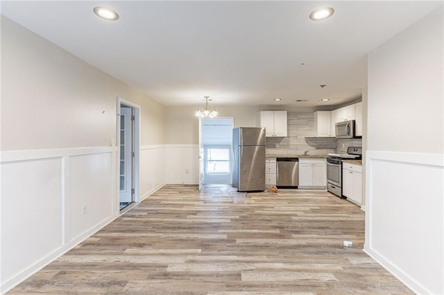 kitchen with a wainscoted wall, appliances with stainless steel finishes, light wood-style flooring, and white cabinets