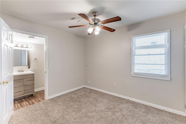 unfurnished bedroom featuring light colored carpet, visible vents, ensuite bathroom, a sink, and baseboards