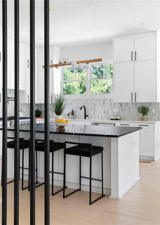 kitchen featuring a breakfast bar area, tasteful backsplash, white cabinets, and light hardwood / wood-style floors