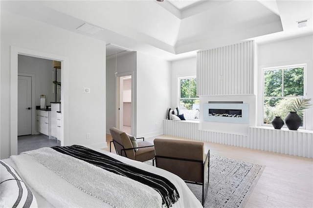 bedroom featuring ensuite bathroom, hardwood / wood-style floors, and a tray ceiling