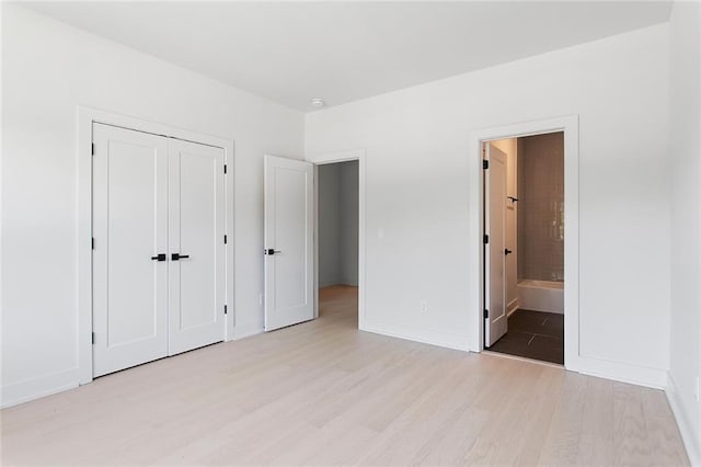 unfurnished bedroom with a closet, ensuite bath, and light wood-type flooring