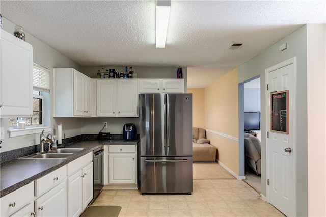 kitchen with dark countertops, appliances with stainless steel finishes, white cabinetry, a sink, and a textured ceiling