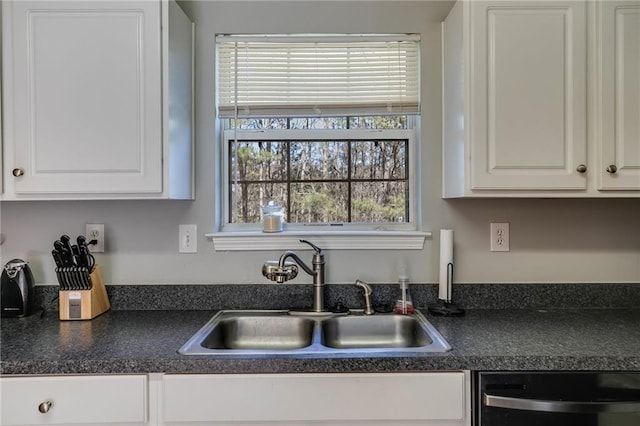 kitchen featuring dark countertops, dishwashing machine, white cabinets, and a sink