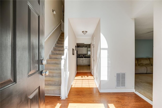 foyer featuring light wood finished floors, baseboards, stairs, and visible vents