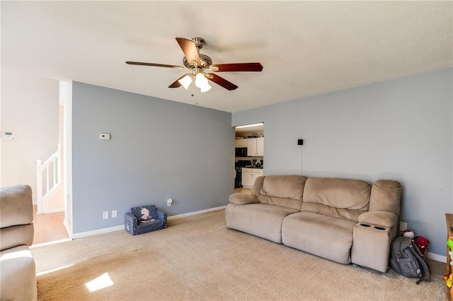 living area with ceiling fan, stairs, baseboards, and light colored carpet