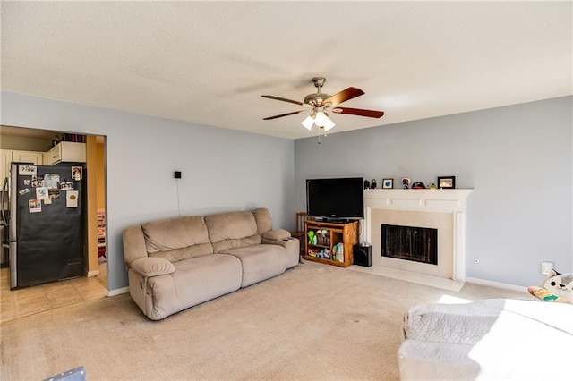 living room with light carpet, a fireplace with flush hearth, baseboards, and a ceiling fan