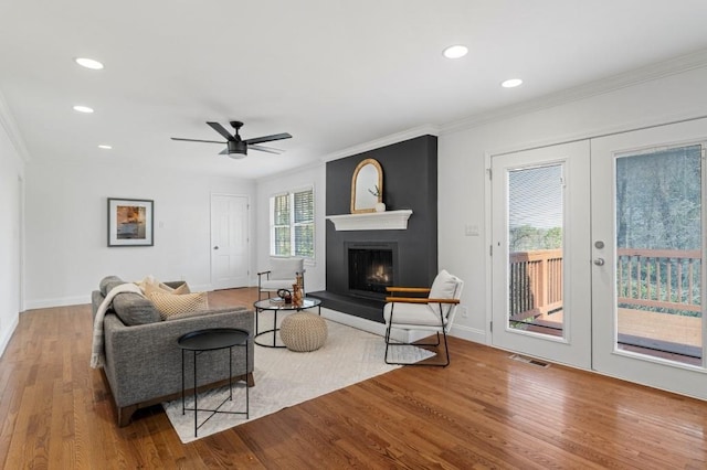 living room with crown molding, light hardwood / wood-style flooring, ceiling fan, a large fireplace, and french doors