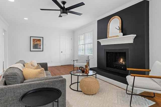 living room featuring crown molding, ceiling fan, wood-type flooring, and a fireplace