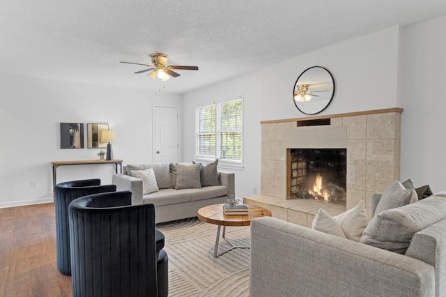 living room featuring a tiled fireplace, ceiling fan, hardwood / wood-style floors, and a textured ceiling