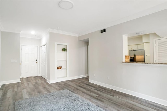 empty room featuring built in shelves, wood-type flooring, and ornamental molding