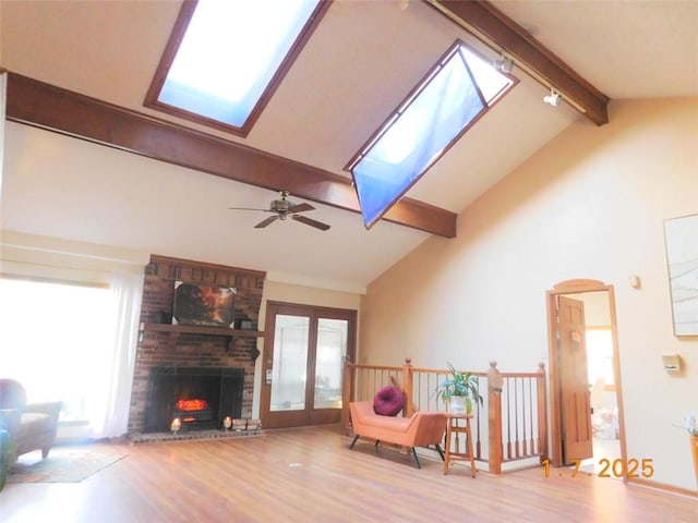 living room featuring wood-type flooring, beam ceiling, a skylight, and a brick fireplace