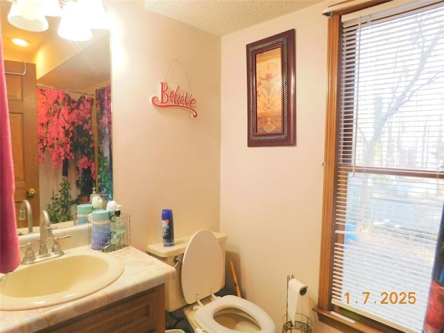 bathroom featuring vanity, toilet, a textured ceiling, and a wealth of natural light