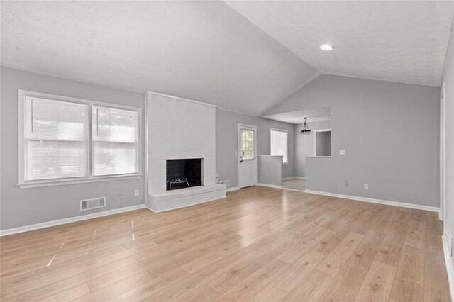 unfurnished living room featuring vaulted ceiling, light wood-type flooring, and a brick fireplace