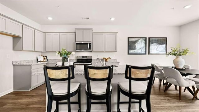 321 Sound Cir, Stockbridge, GA 30281 - kitchen with appliances with stainless steel finishes, gray cabinetry, a center island with sink, dark wood finished floors, and light stone counters