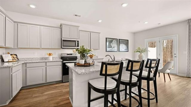 321 Sound Cir, Stockbridge, GA 30281 - kitchen featuring appliances with stainless steel finishes, gray cabinetry, a center island with sink, light stone counters, and a breakfast bar