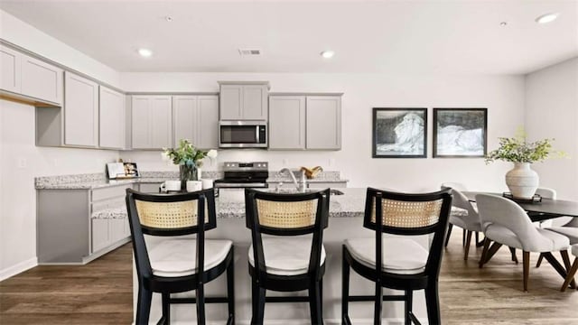 321 Sound Cir, Stockbridge, GA 30281 - kitchen with stainless steel appliances, gray cabinets, a kitchen island with sink, dark wood-type flooring, and light stone countertops