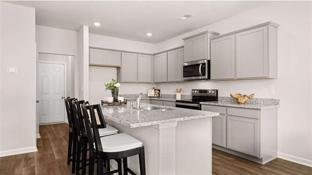 321 Sound Cir, Stockbridge, GA 30281 - kitchen featuring appliances with stainless steel finishes, gray cabinets, dark wood-style floors, an island with sink, and light stone counters