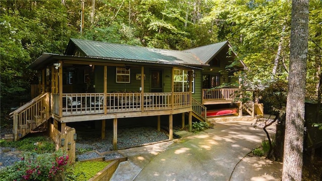 view of front of house featuring stairway, a porch, metal roof, and a forest view