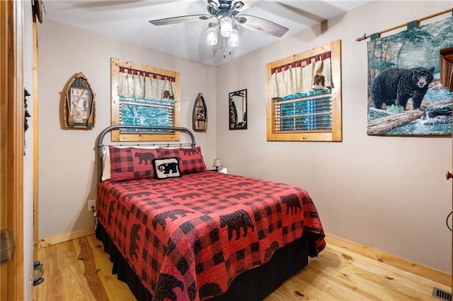 bedroom with ceiling fan, wood finished floors, visible vents, and baseboards